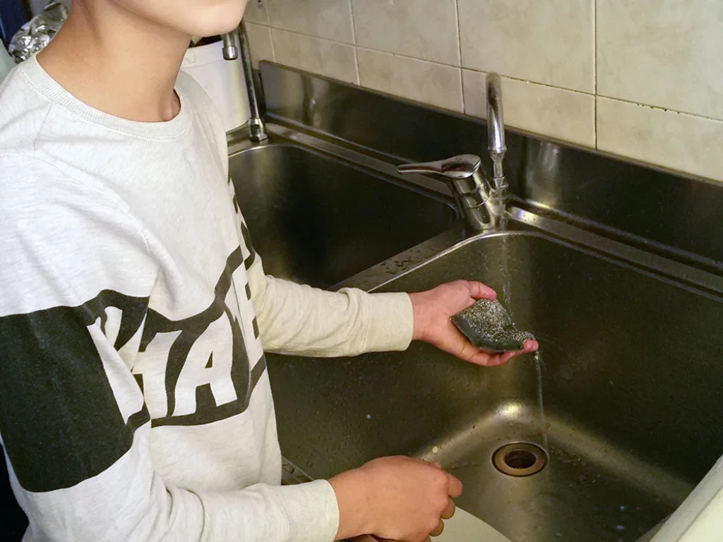 Ein Jugendlicher wäscht an einem Spülbecken ab.